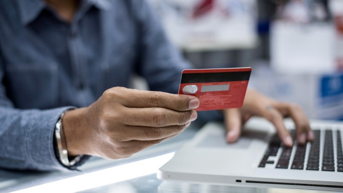 A man holds a red credit card in one hand while using a laptop with the other.